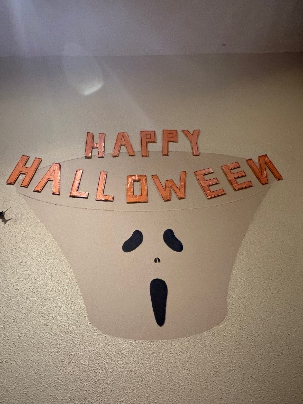 壁に手作りの文字で「HAPPY HALLOWEEN」と書かれた、おばけの顔の飾り
