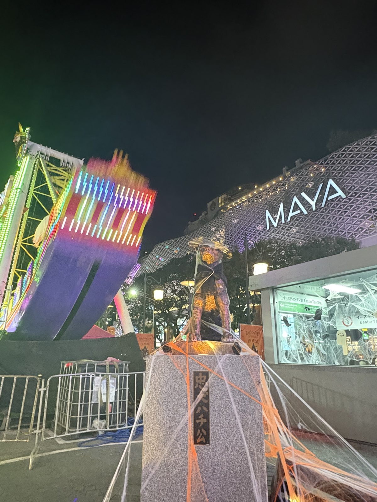クモの巣をかけられ、帽子をかぶせられた「忠犬ハチ公」の像。うしろにはバイキングと MAYA の建物