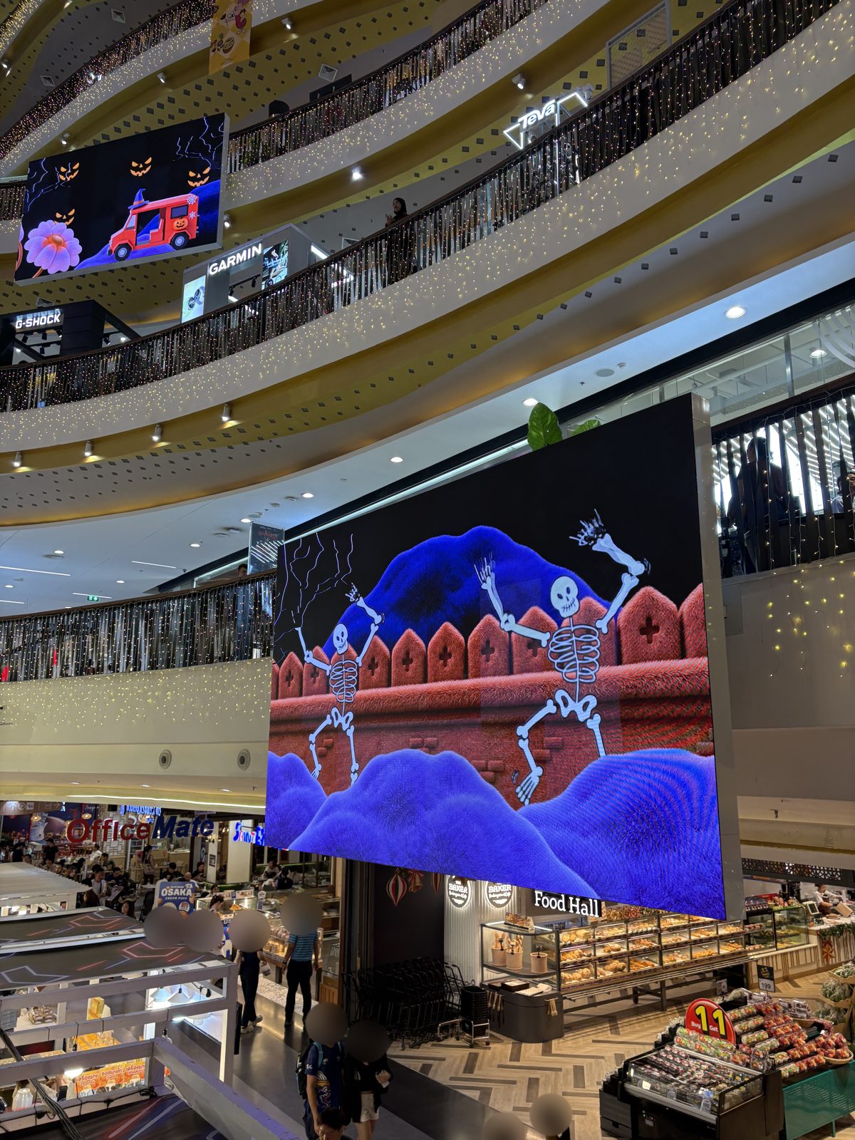 吹き抜けの大きな画面に映る、赤い塀の上で踊る骸骨のアニメーション。上の画面にはカボチャを積んだ赤い車