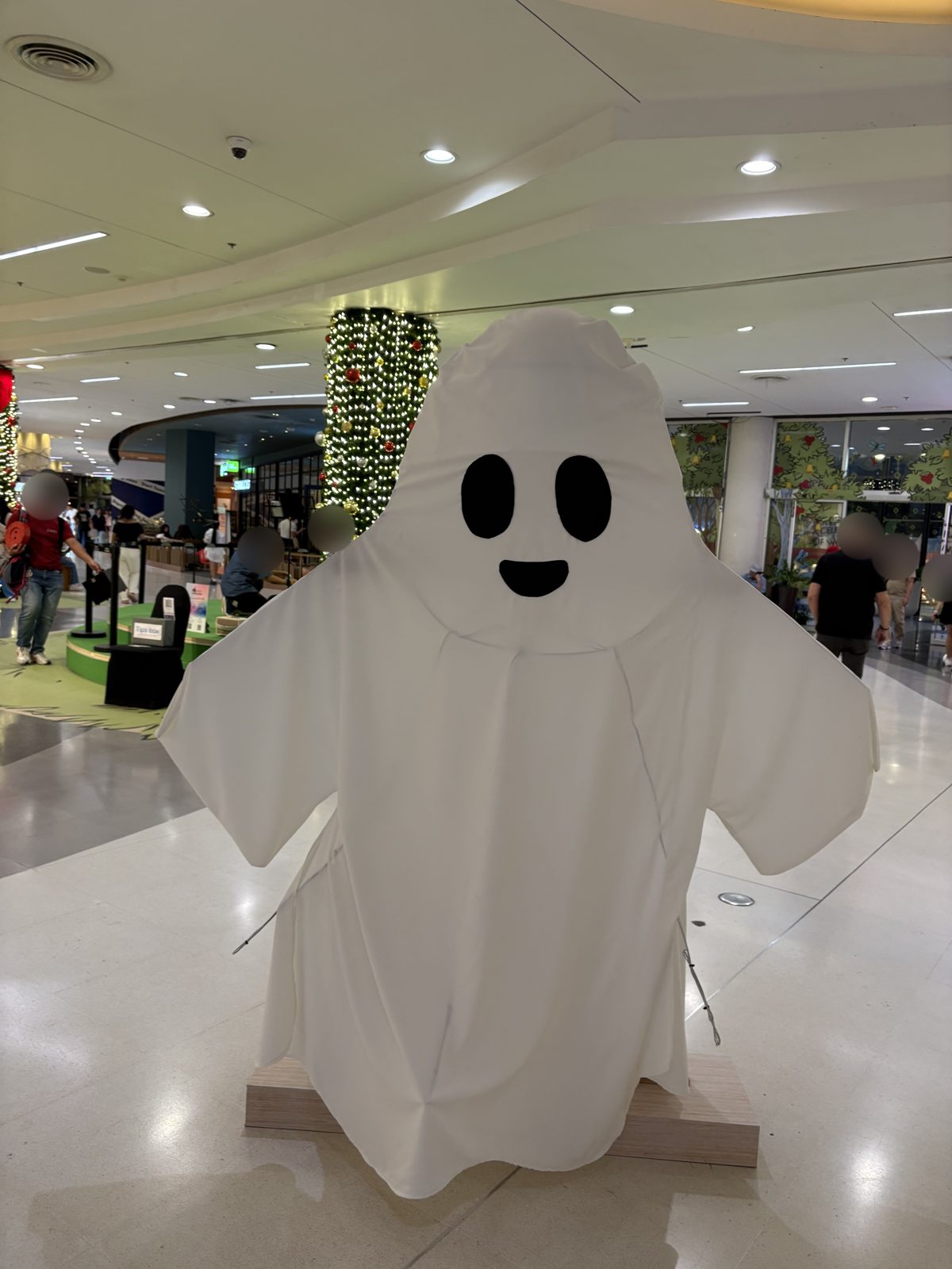 モールの通路に立つ、白い布でできたにこにこ顔のおばけ。うしろの柱にはクリスマスのような飾り